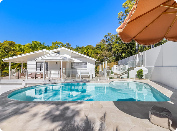 Modern backyard pool with white house and large umbrella in sunny outdoor setting.
