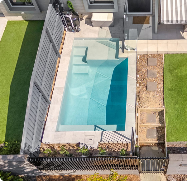 Concrete plunge pool with steps and surrounding patio in backyard.